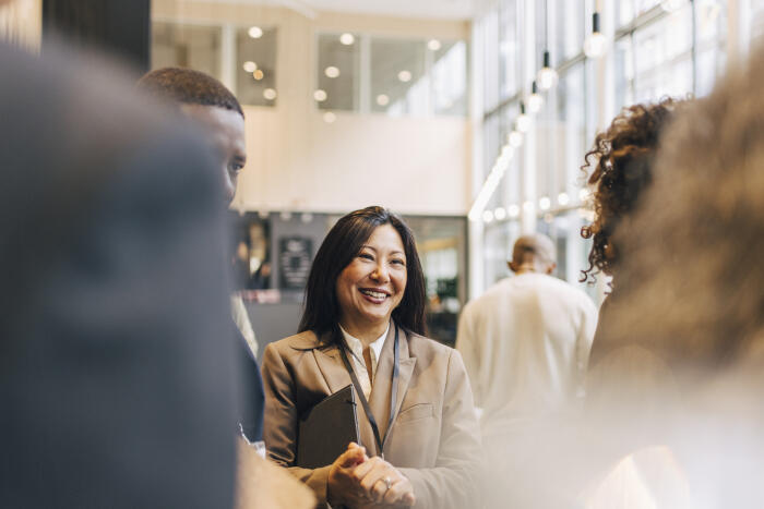 Happy mature businesswoman with hands clasped discussing with delegates at convention center