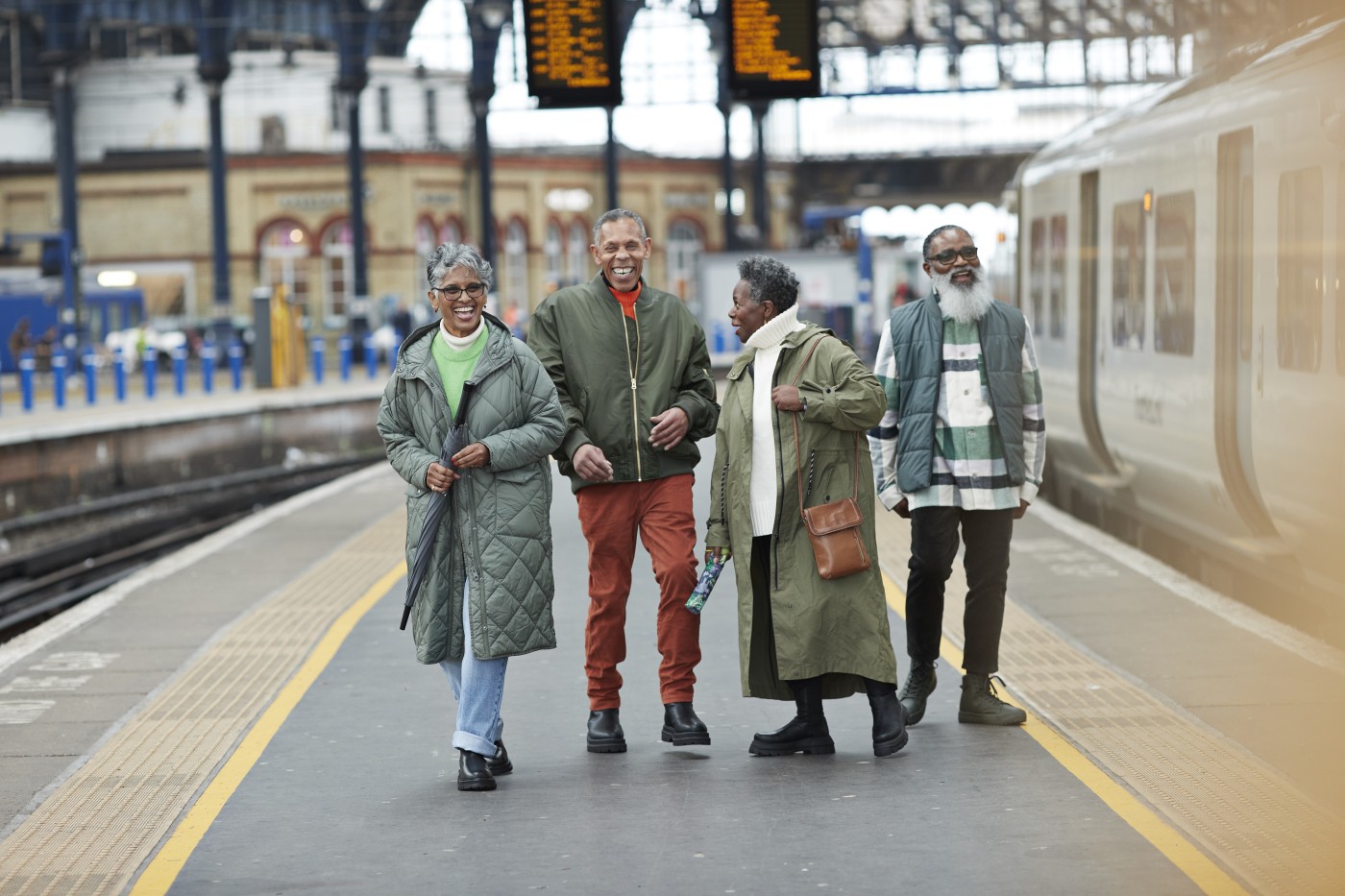 Happy senior male and female friends talking while walking at railroad station platform during vacation