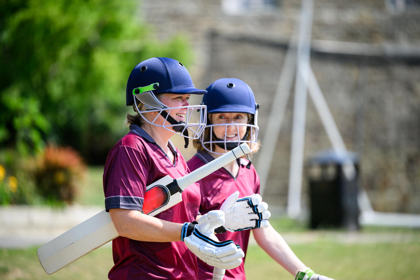 Mixed age range and ethnicity women and girls cricket teams playing match together outdoors in summer