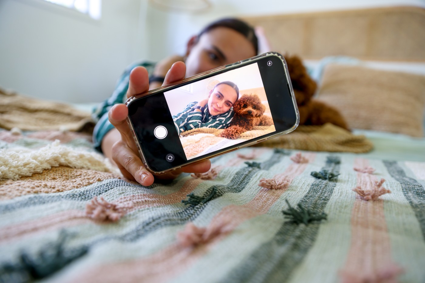 Teenager on bed with their pet dog looking at digital device