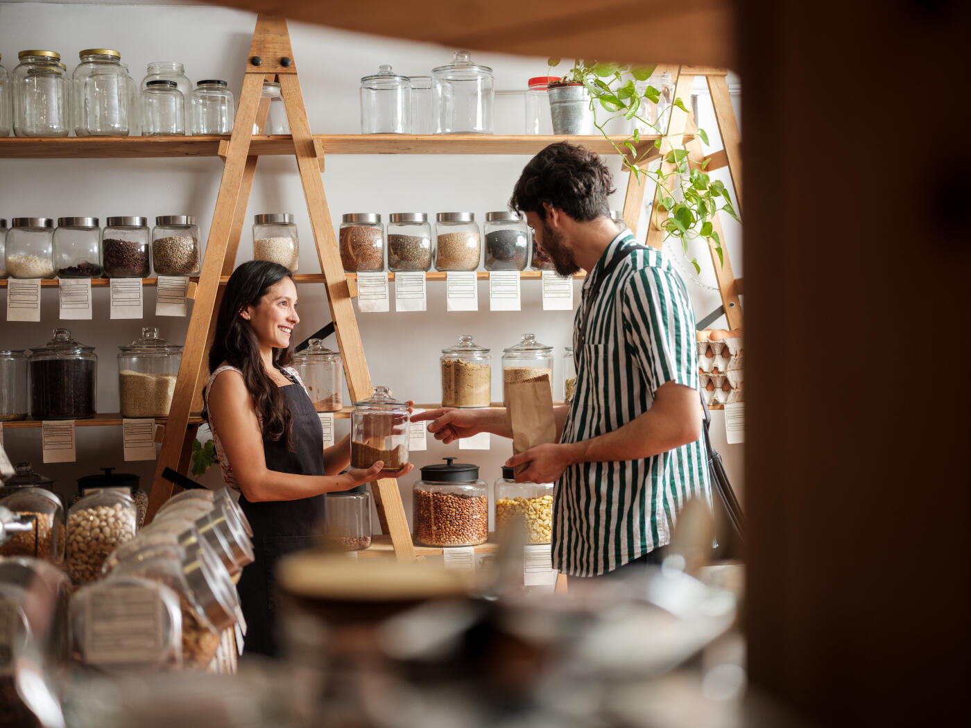 A happy hispanic employee helping a young man in a zero waste store.