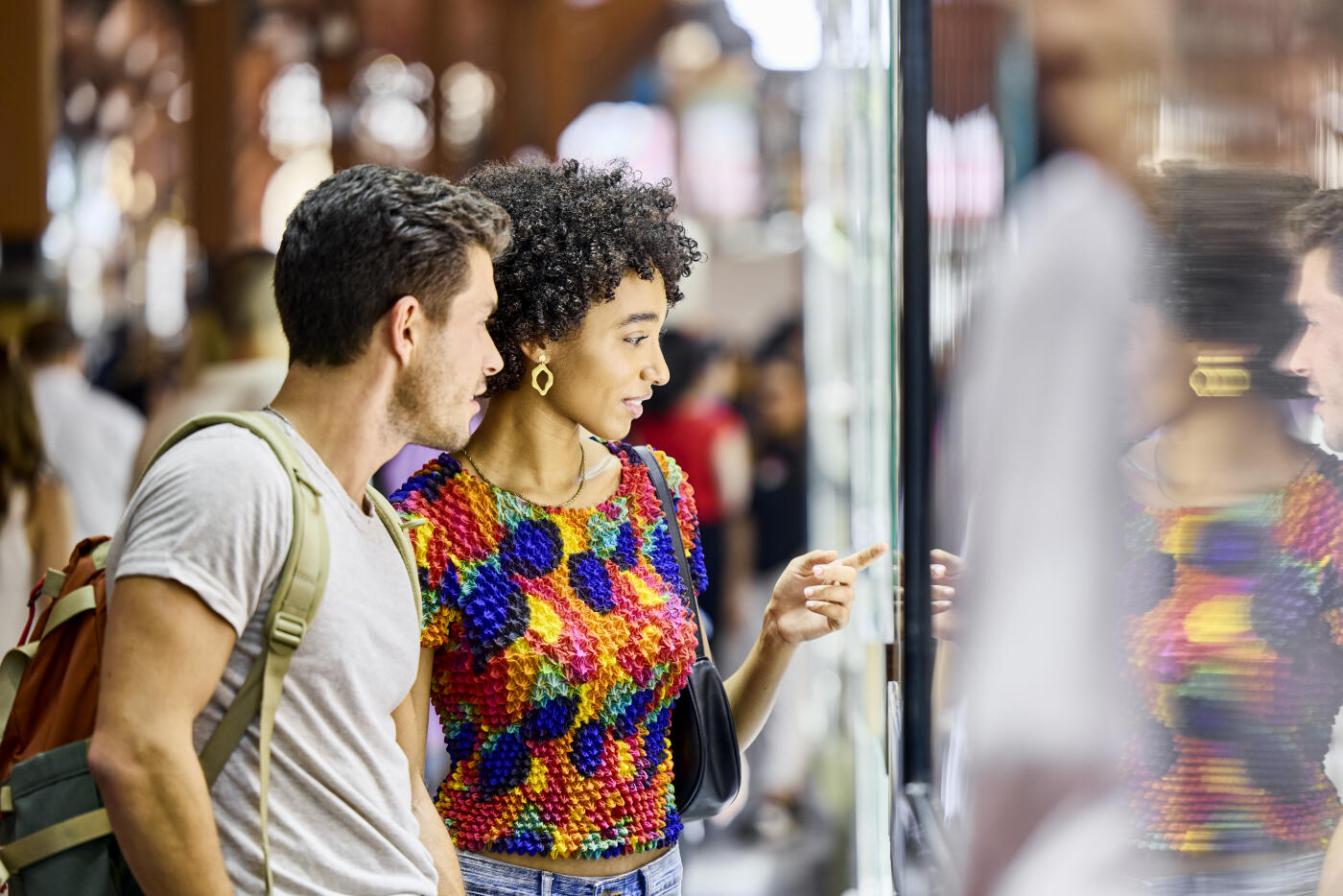 Girlfriend doing window shopping with man. Couple are exploring local market. Woman is pointing at display.