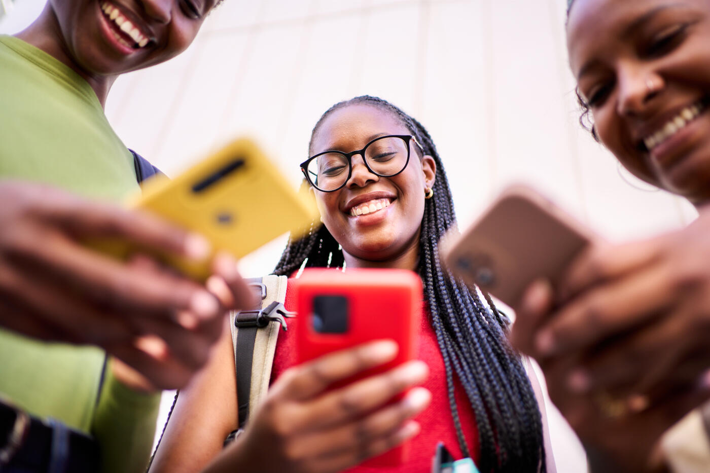 Cheerful group of three African women gathering together using cellphones outdoors with a low angle view.