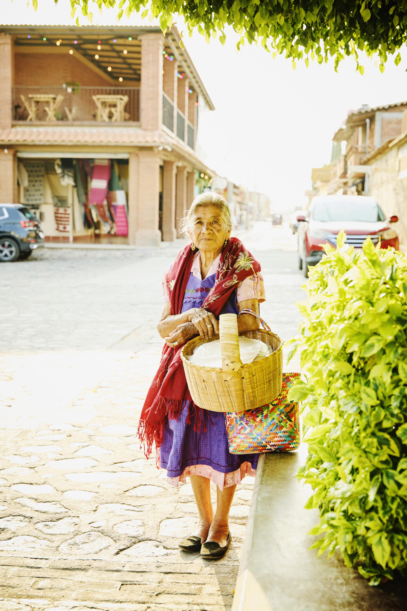 Wide portrait shot of senior female street food seller carrying  a basket of her homemade tostadas in small provincial town