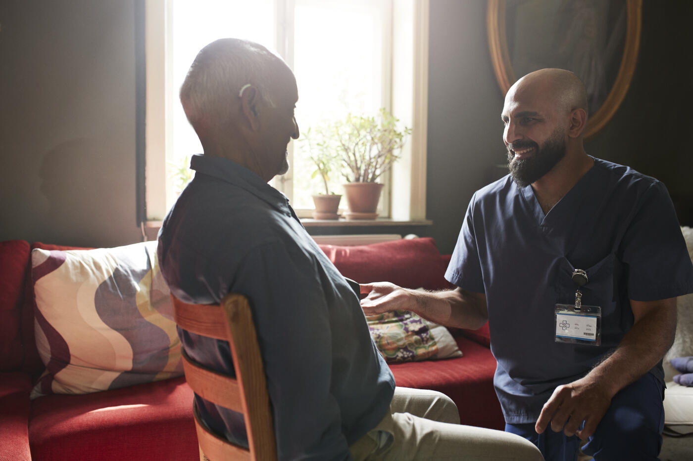 Smiling male nurse talking with senior man sitting on chair in living room