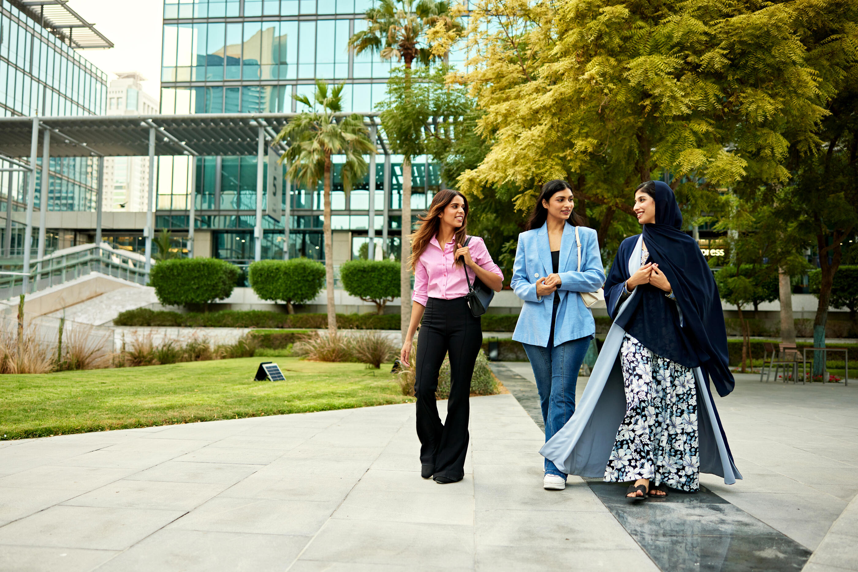 Full length view of young office workers walking side by side through plaza with modern office buildings in background.