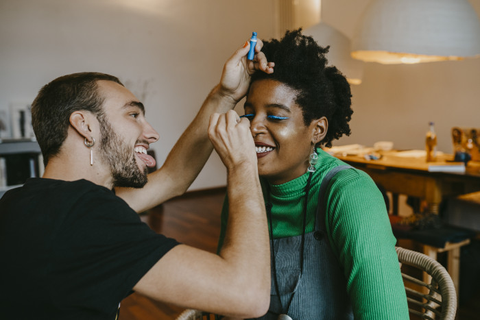Smiling man applying blue eyeliner to female friend at home