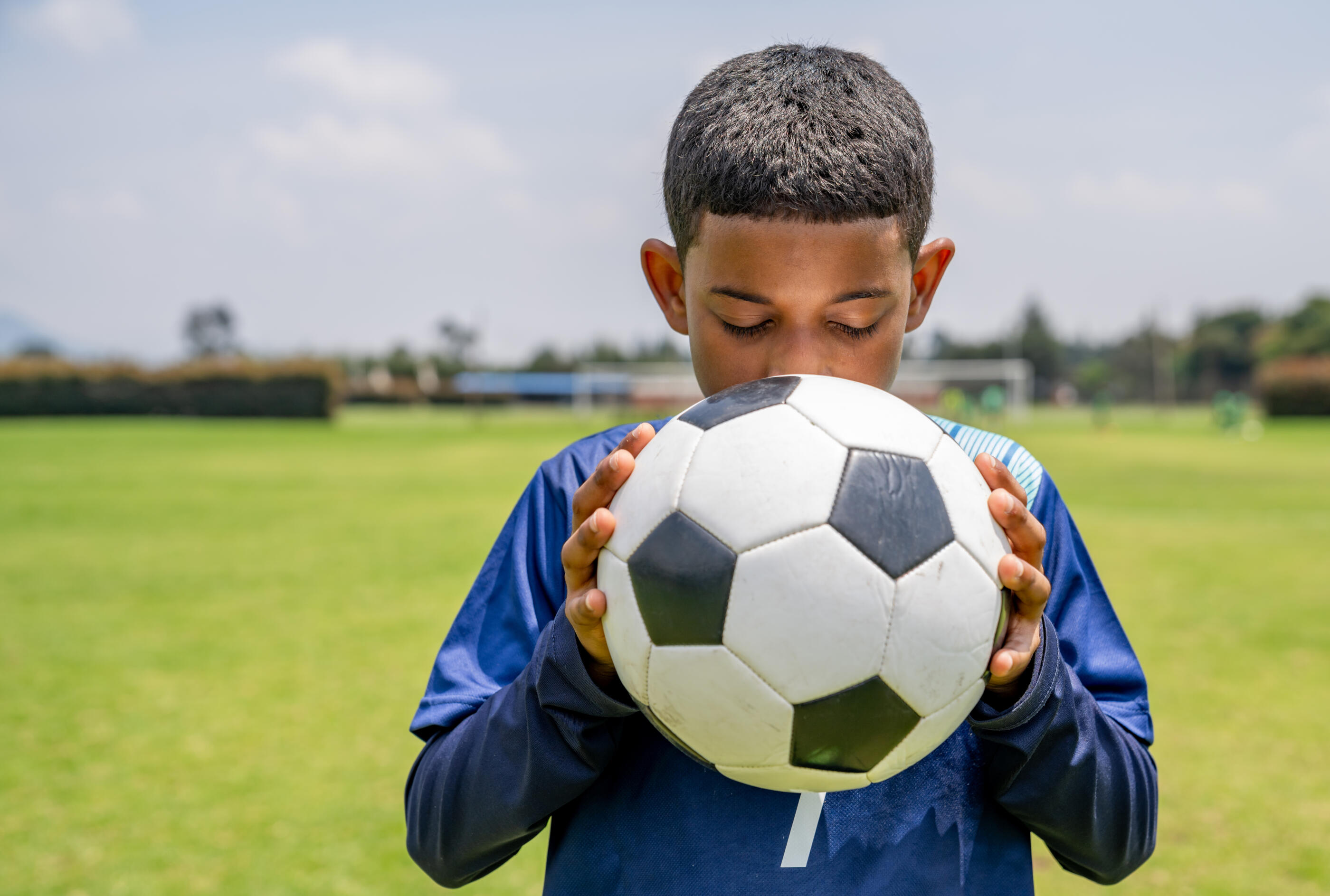 Portrait of a focused young football player holding a soccer ball at the field and closing his eyes