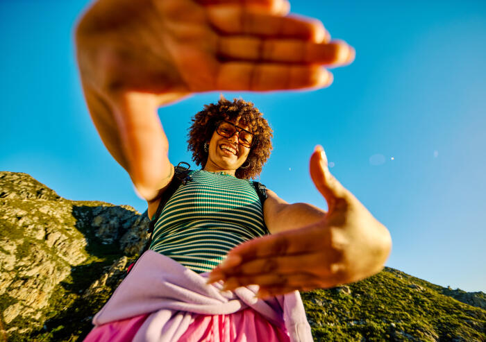 Young female hiker framing scenic mountain view with hands during sunny hike