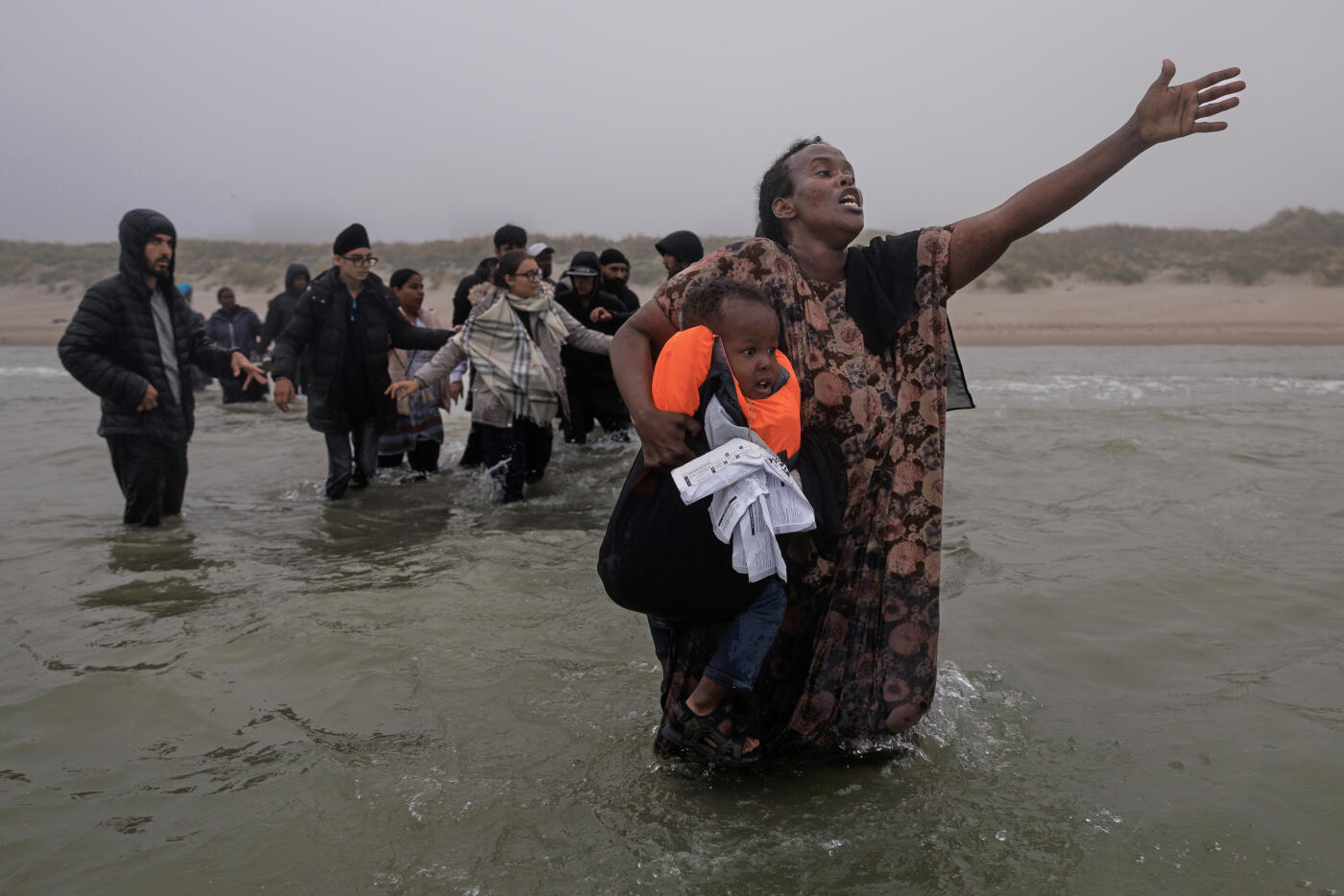 GRAVELINES, FRANCE - JULY 02: A woman holding her child pleads with traffickers to be let onto a small boat as it arrives on the shore to collect more people in the thick fog on July 02, 2025 in Gravelines, France. The boat had arrived through the fog, already very full of migrants who had boarded further down the coast, looking to squeeze a few more people in. Last month, it was reported that French officials were planning changes to policies that govern interceptions at sea, allowing police to intercept small boats within 300 metres of the French shoreline, in a bid to curb migrant crossings of the English Channel. The move, which has not been confirmed, would be welcomed by UK authorities, who see it as a step toward stronger border enforcement. (Photo by Dan Kitwood/Getty Images)