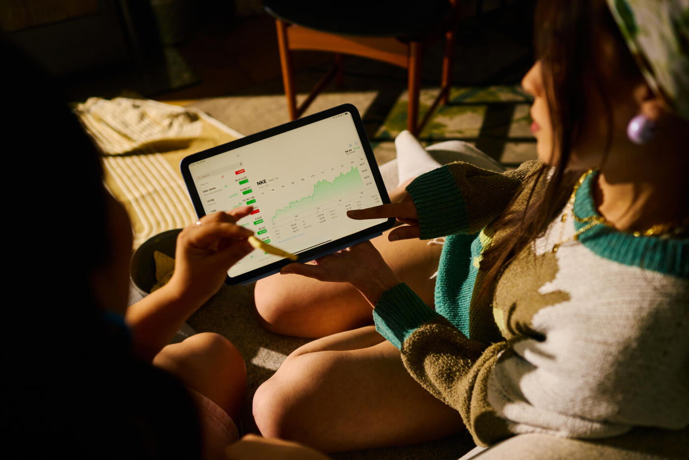 Young female friends discussing finance, investing, and economic growth indicators on a digital tablet