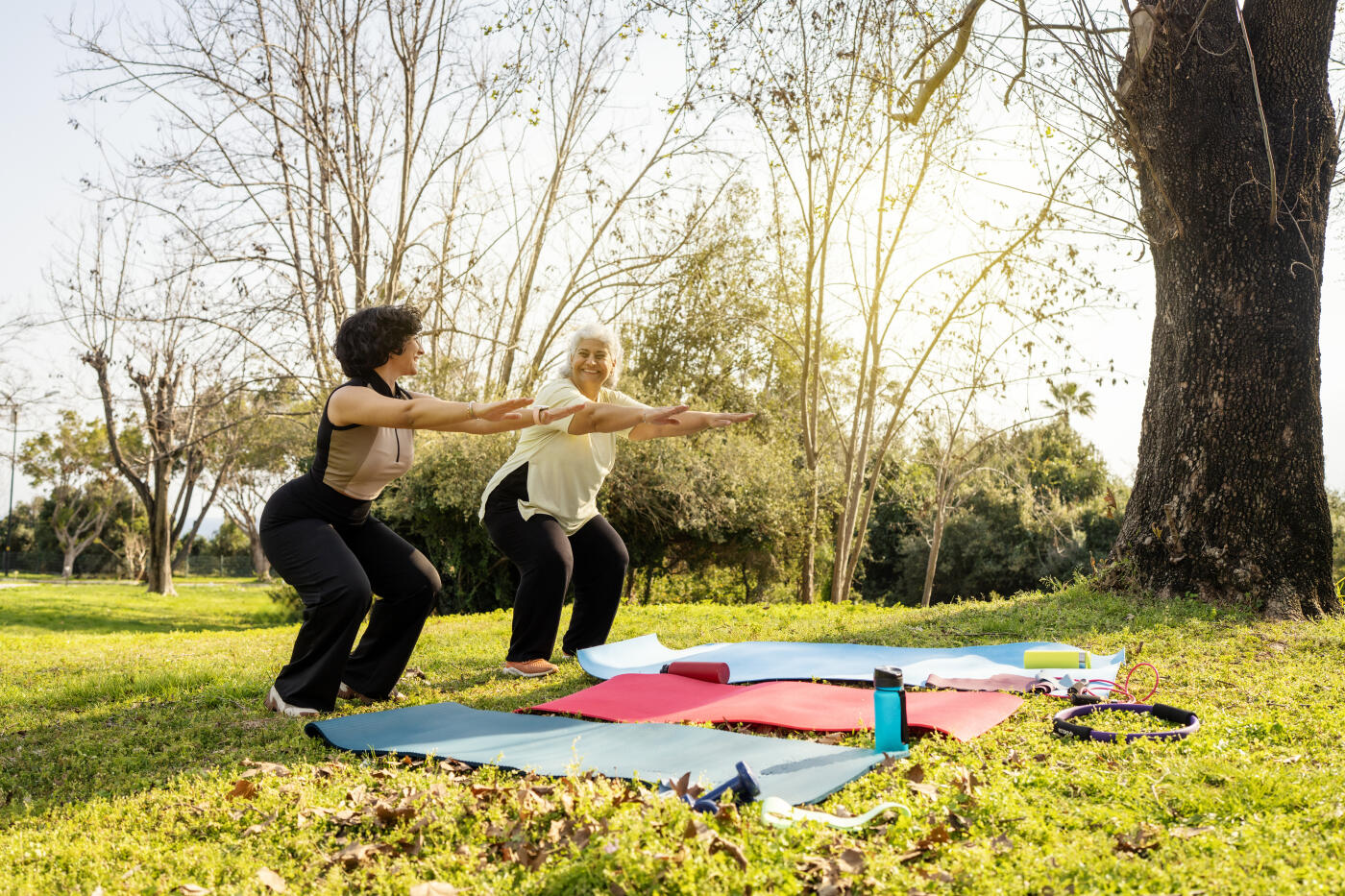 Portrait of a senior mother with grey hair and her adult daughter working out together in a lush green park