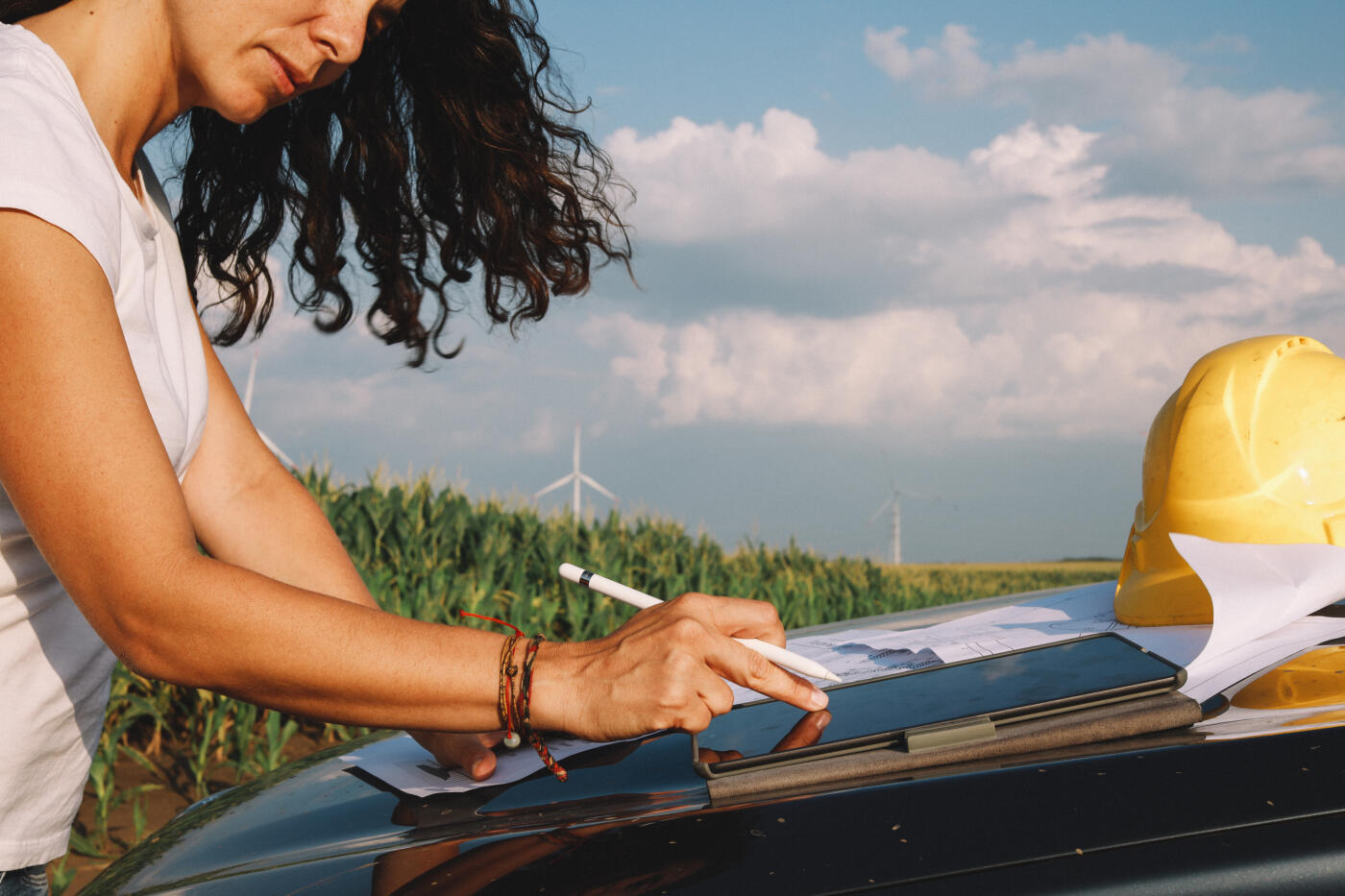 Female scientist working in the field, inspecting wind turbine efficiency. She is checking blueprints and real time inspection via digital tablet.