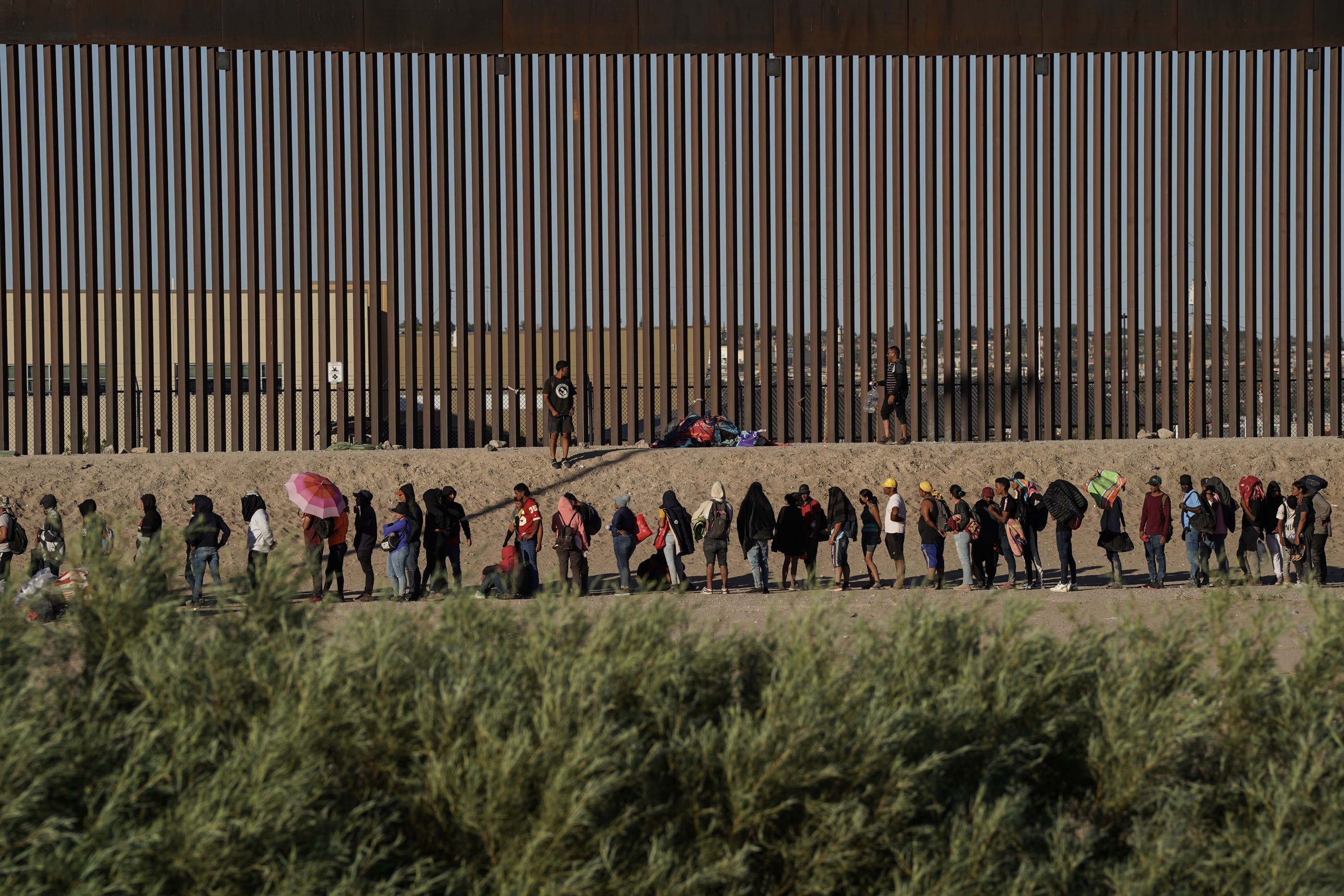 CIUDAD JUAREZ, MEXICO - SEPTEMBER 19, 2023  Migrants line up to be processed by US Border Patrol Agents along the border wall separating the US from Mexico on September 19, 2023 in Ciudad Juarez, Mexico. In the past few days there has been a surge of migrants along the border. Mexican railway operator Ferromex has suspended service due to deaths and injuries from the many migrants that use the cargo trains as transportation. Thousands have been riding atop the trains. (Photo by Michael Robinson Chávez/The Washington Post via Getty Images)
