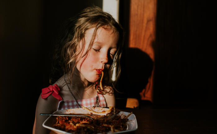 Comical image of a sleepy little girl sucking spaghetti