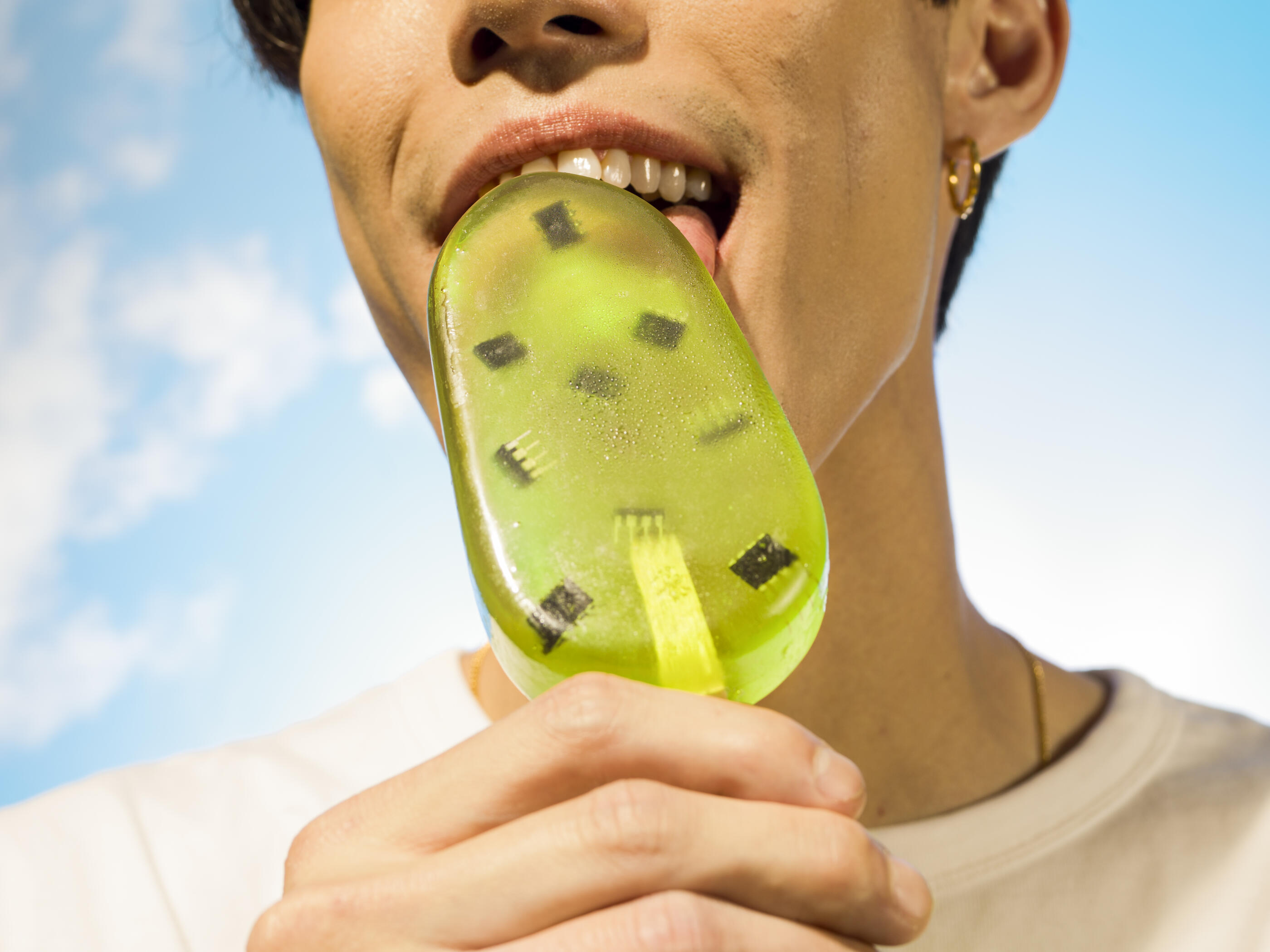 Low angle close up of young man licking translucent green popsicle filled with microchips