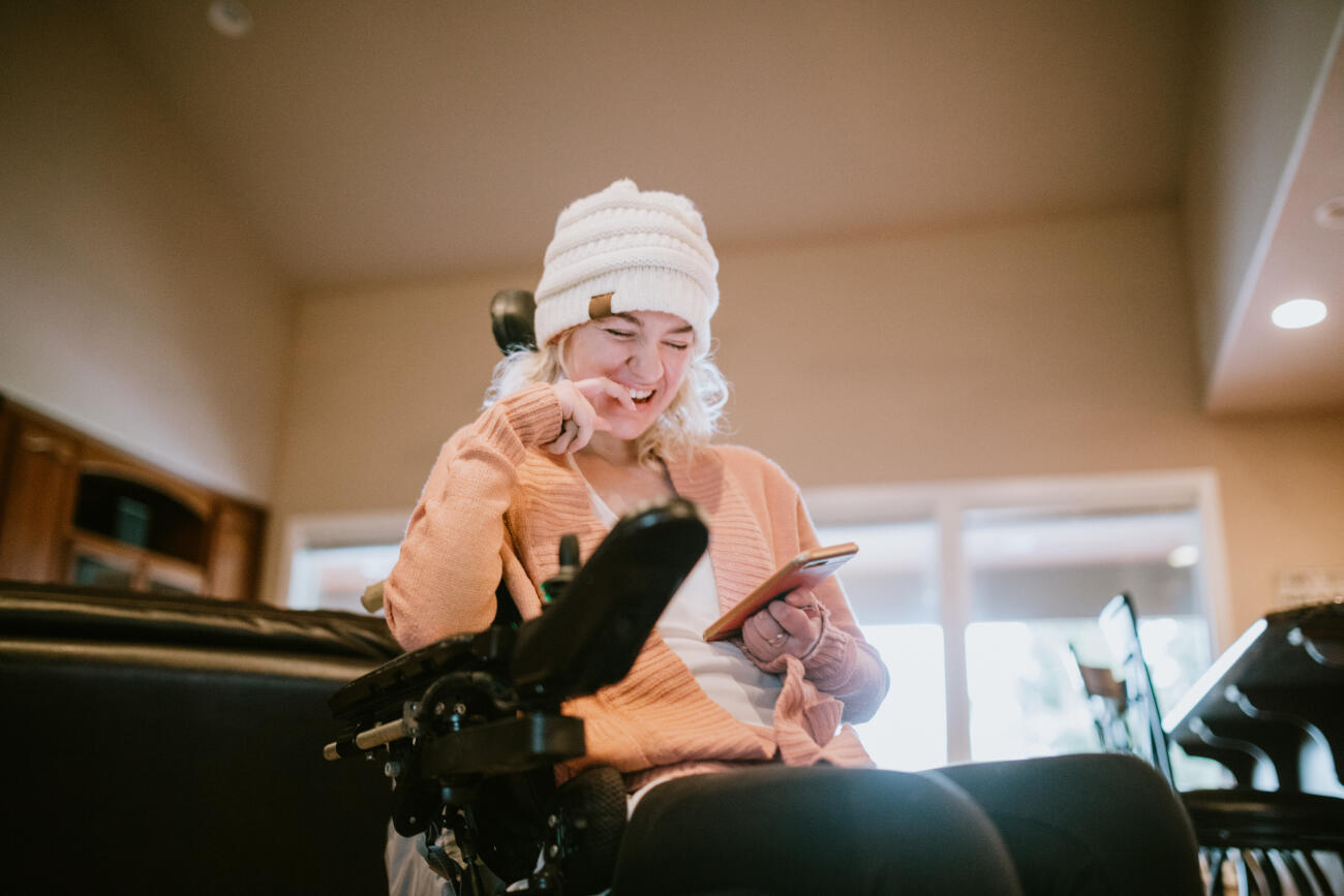 An independent young adult woman with cerebral palsy going about some of her daily routines at home.  She smiles while browsing social media apps on her phone.