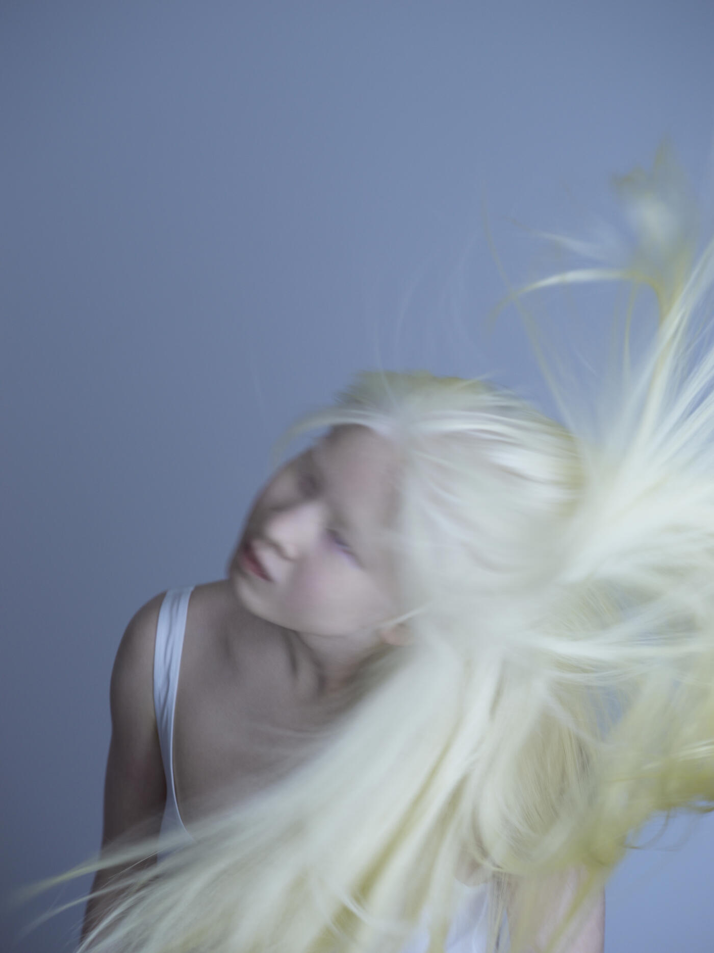 Albino Chinese young teenage female, with blonde hair, facing left, shaking her hair, wearing a white vest top.