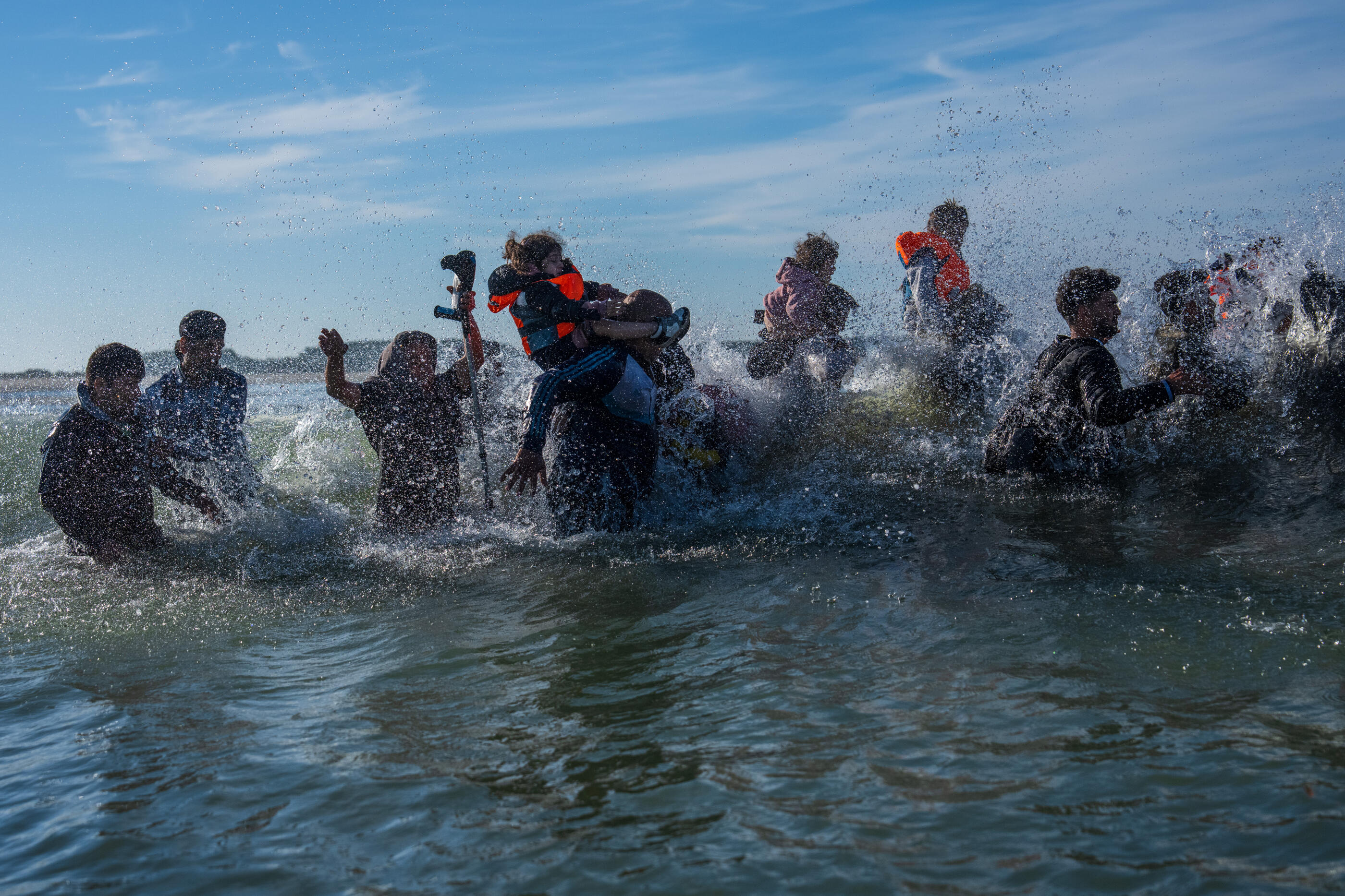 GRAVELINES, FRANCE - AUGUST 25: A little girl falls off a man's shoulders as they are hit by a wave while waiting to board a dinghy into the English Channel on August 25, 2025 in Gravelines, France. Migrant crossings by boat have caused much controversy in the UK, with far-right groups organising demonstrations outside hotels housing migrants across the country over the summer. As of late August 2025, more than 28,000 migrants have crossed the English Channel in small boats this year. (Photo by Carl Court/Getty Images)
