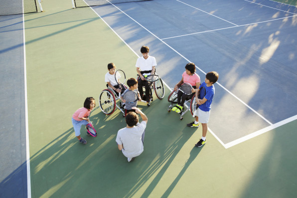 A tennis coach having a meeting with young students, some in a wheelchair and some standing