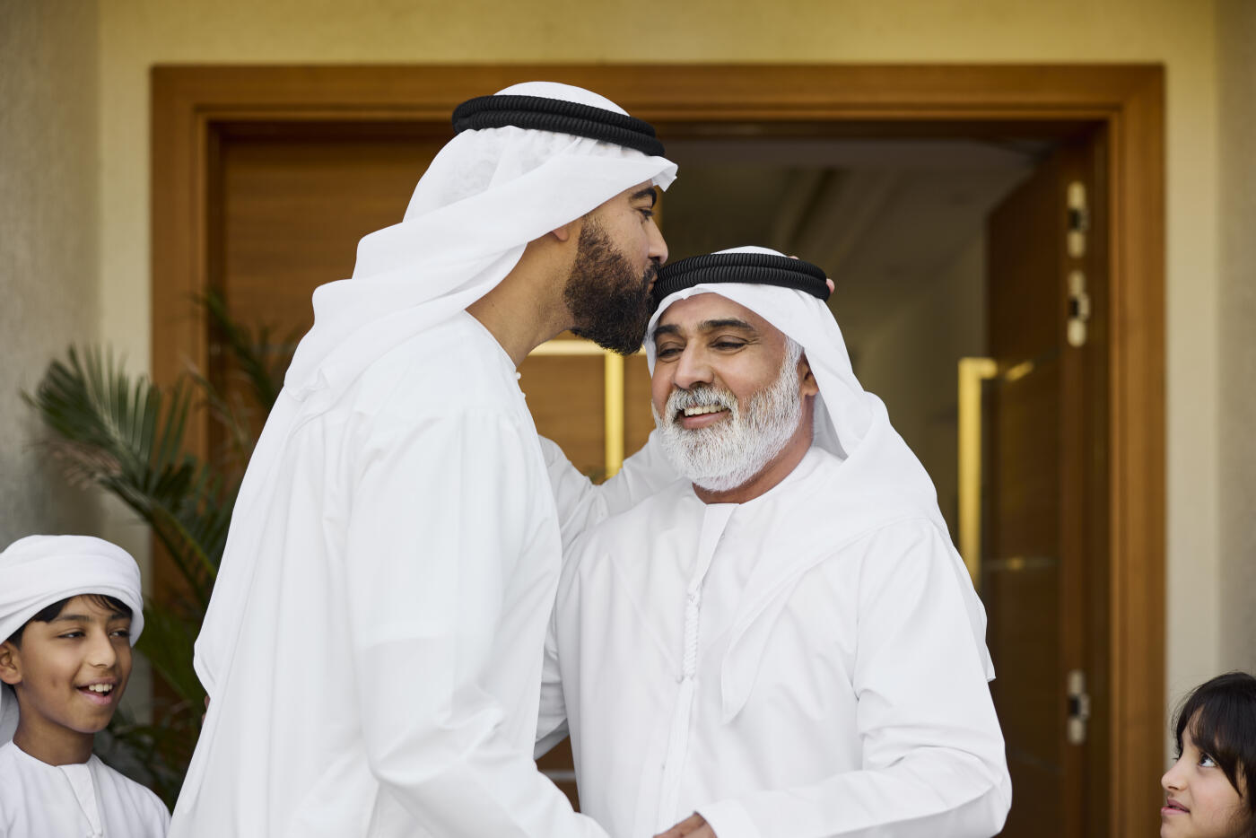 Middle eastern male kissing on man's forehead outside house. Happy Saudi men greeting each other. They are honoring their cultural origins.