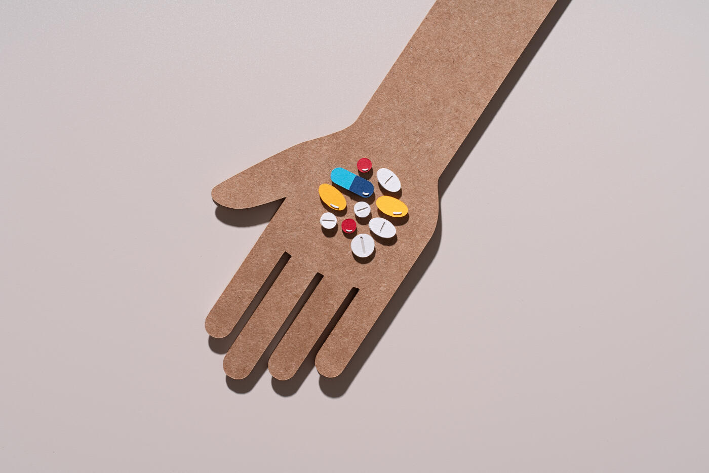 Paper Craft Hand Holding Multiple Pills and Capsules on Brown Background Directly above View.