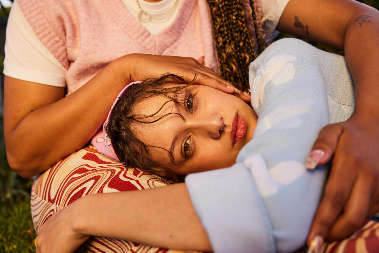 Young woman looking at camera with head on partner's lap, woman gently touching her head