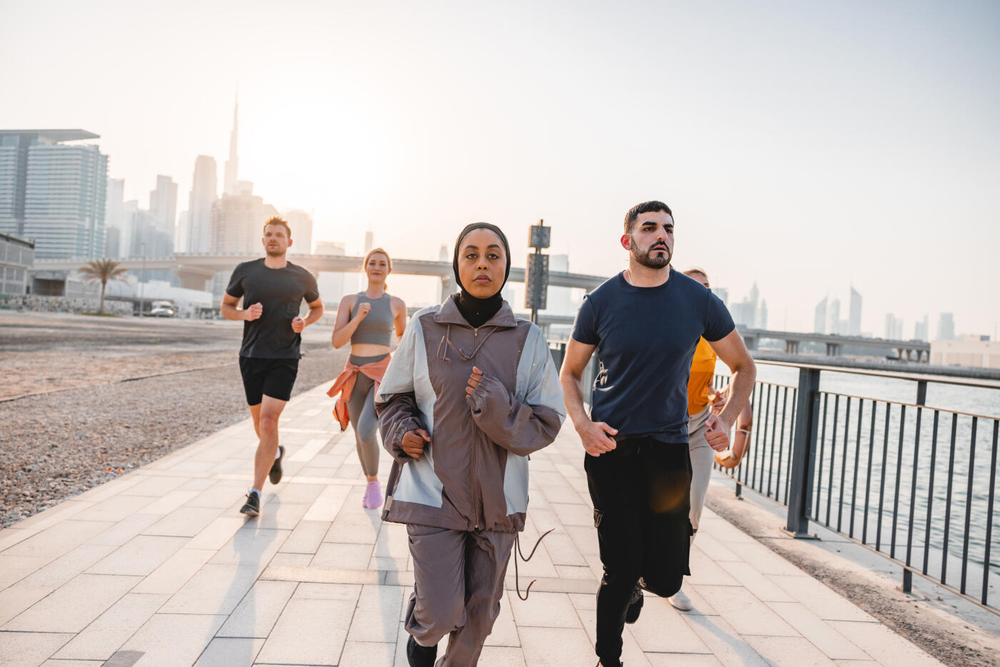 Team Of Multiracial Young Adult Athletes Warming Up Running Around The City At Sunset In Dubai.
