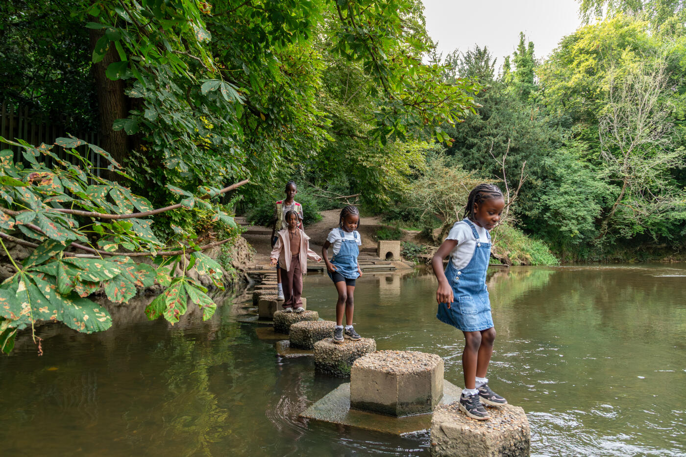 our young Black children explore stepping stones beside a stream during a hike at Box Hill, Surrey.
