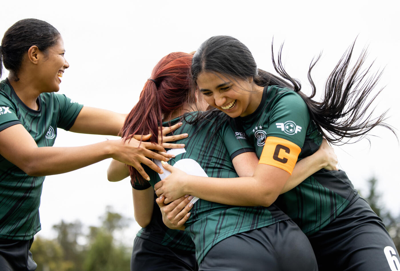 Happy Latin American female soccer players celebrating a victory at the field and hugging