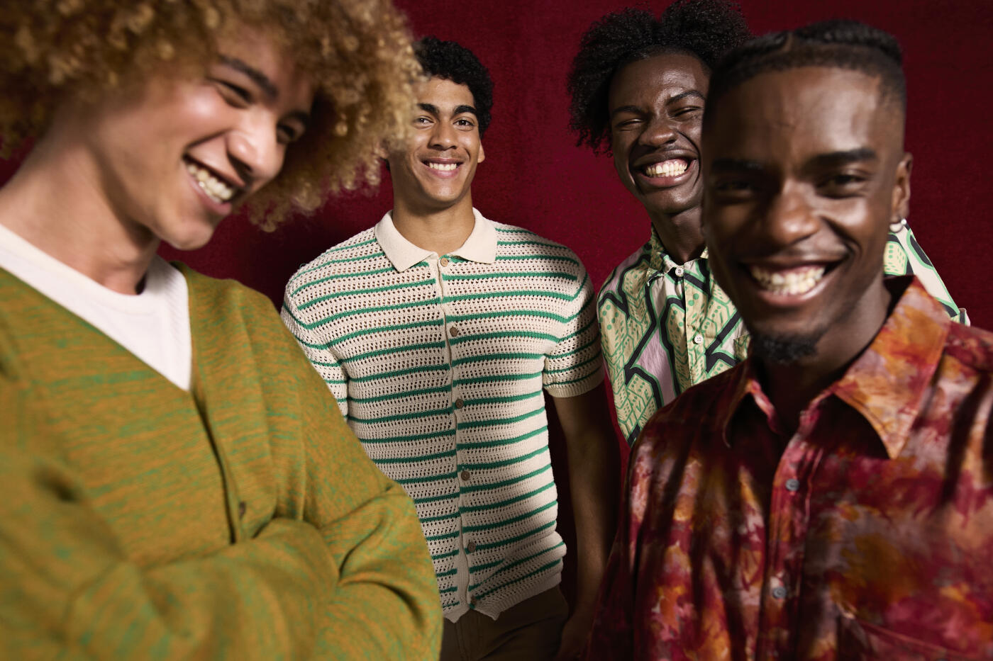 Portrait of happy young men standing with androgynous friend against maroon background