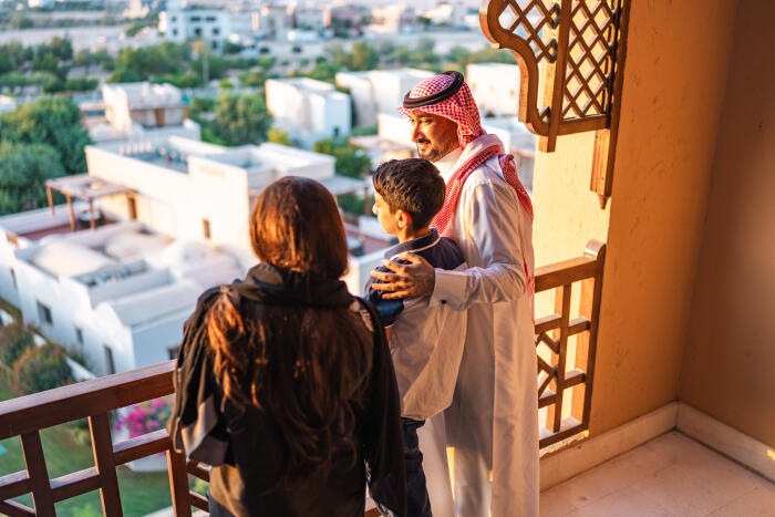 Arab Father and Son Admiring Cityscape View from Hotel Balcony During Golden Hour