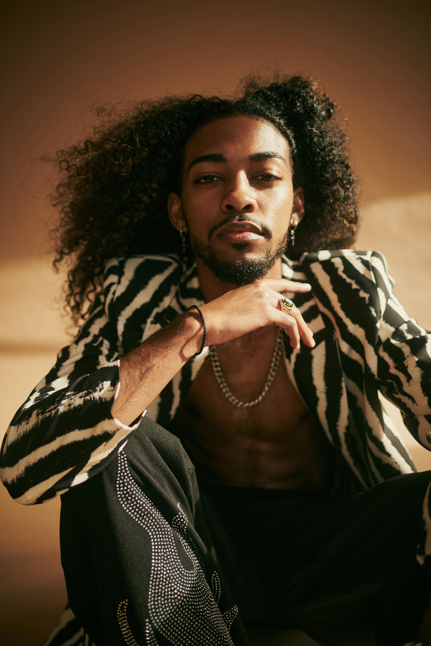 A male model with long curly hair shot against a brown studio backdrop wearing fashionable clothing - stock image - stock image