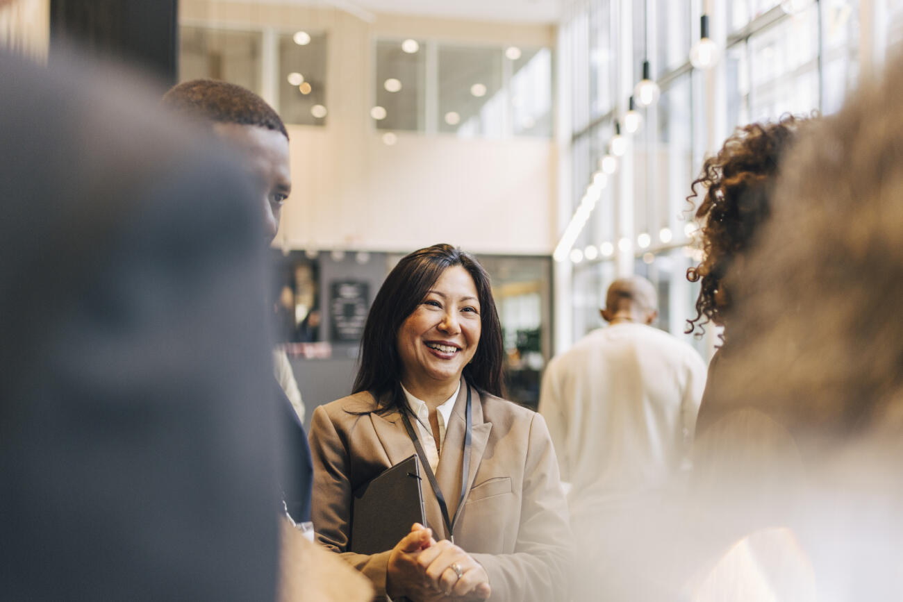 Happy mature businesswoman with hands clasped discussing with delegates at convention center