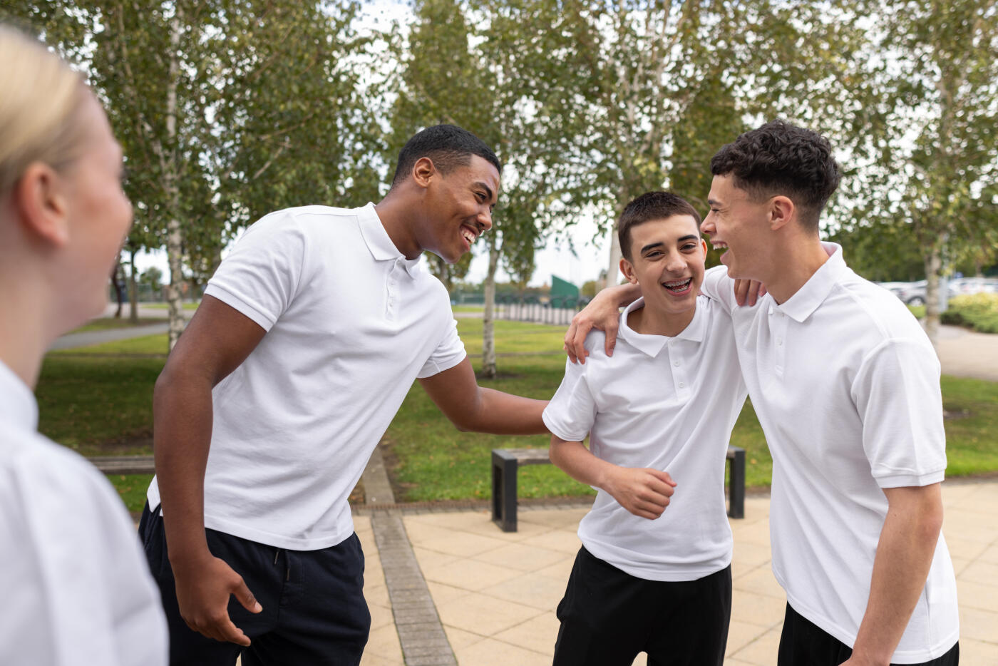 Group of teenagers standing outside of a school talking together in the North East of England. They are all wearing polo shirts, standing talking together outside of their school reception area.  The boys are laughing while putting their arms around each other. Videos are available similar to this scenario.