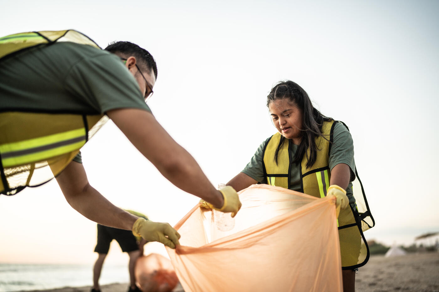 Recyclers picking up trash and putting in the plastic bag at beach - including special need young woman