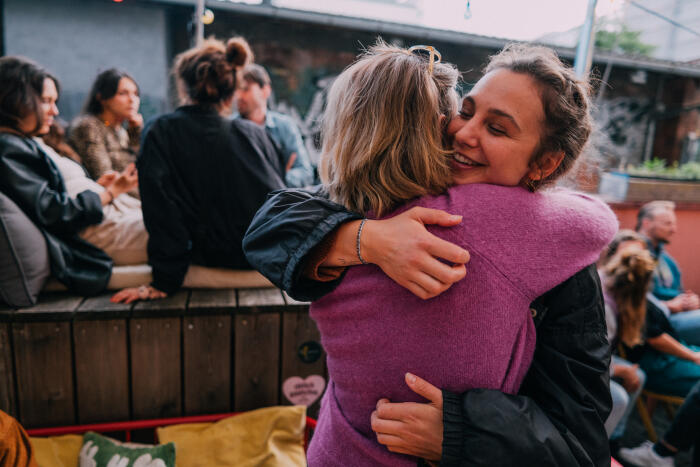 Two Female Friends Embracing Warmly at a Social Gathering Outdoors