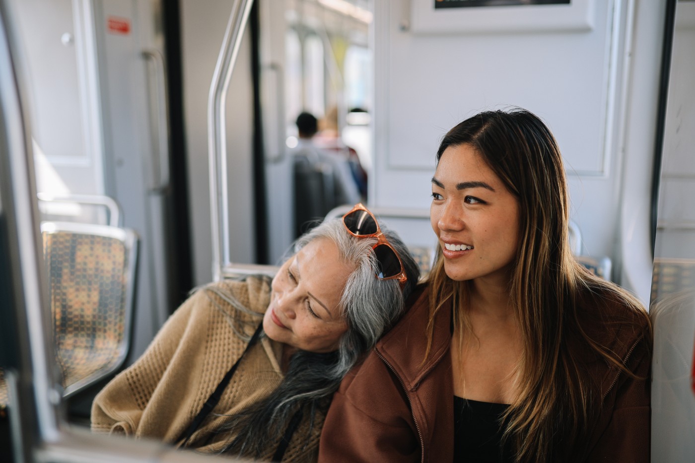 Mom and daughter going for a staycation in California, using sustainable ways of traveling. They are using the Pacific train lines and Los Angeles commuter trains for a quick nature getaway together, sitting in the train together. Mom is tired and she is sleeping on her daughter’s shoulder.