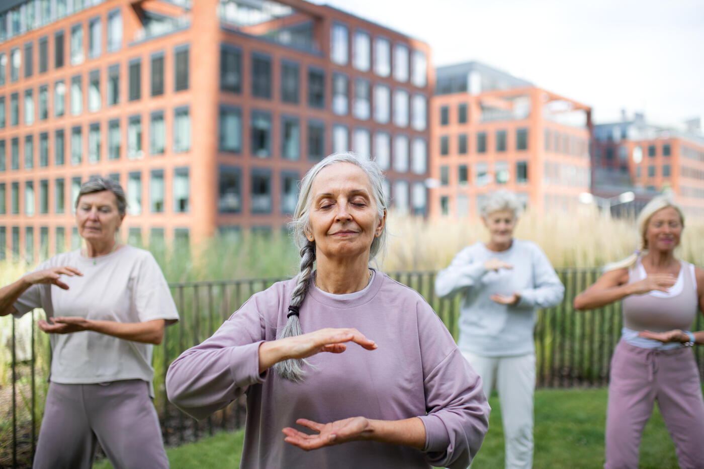Group of senior women friends doing tai chi exercise outdoors in town park.