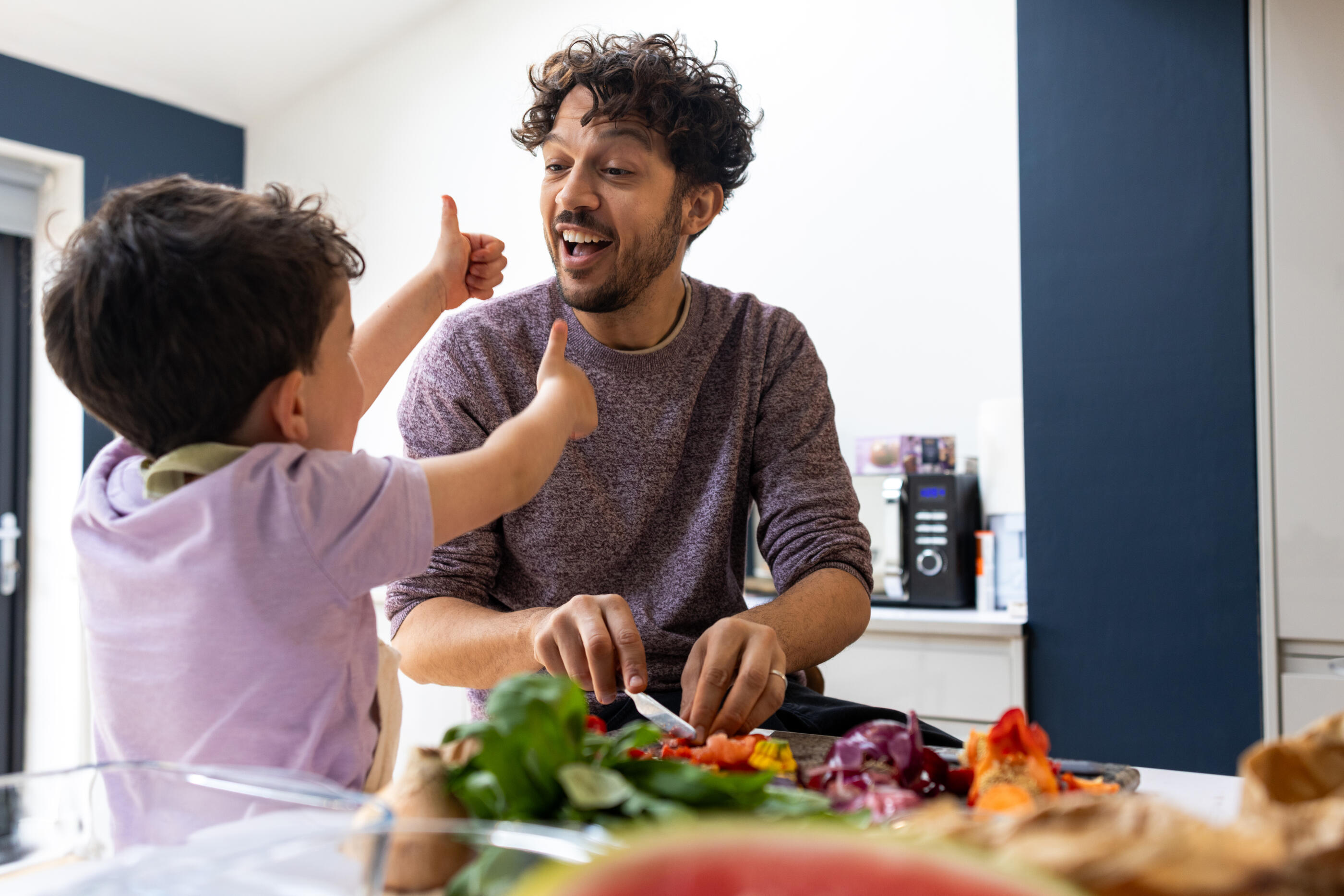 A medium shot of a father and young son preparing fresh vegetables together in a modern kitchen. The father is chopping colourful produce for a healthy meal. A scene of family bonding and a healthy lifestyle at home. The son is sticking his thumbs up at his father while the father smiles at him with pride.

Videos are available similar to this scenario.