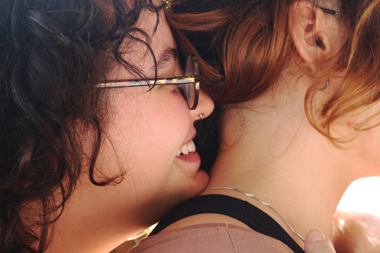 The girl approaches her girlfriend's neck with her breath and her smile. An intimate scene, full of love and affection.