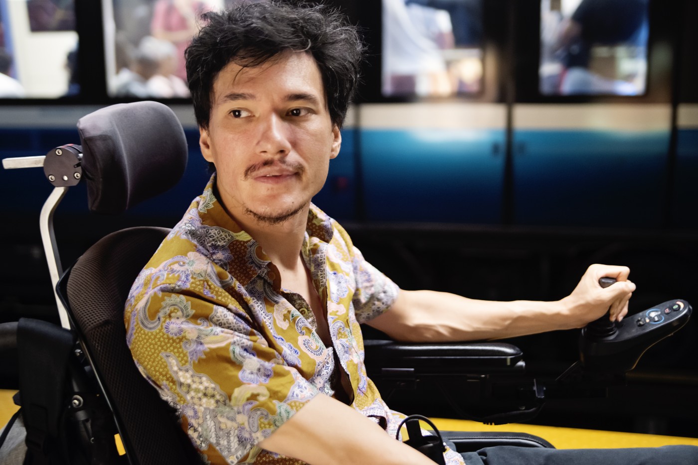 Young asian man using a wheelchair in a subway station. He has cerebral palsy and wheelchair is motorised. Horizontal waist up indoors shot with some copy space. This was taken in Montreal, Quebec, Canada.