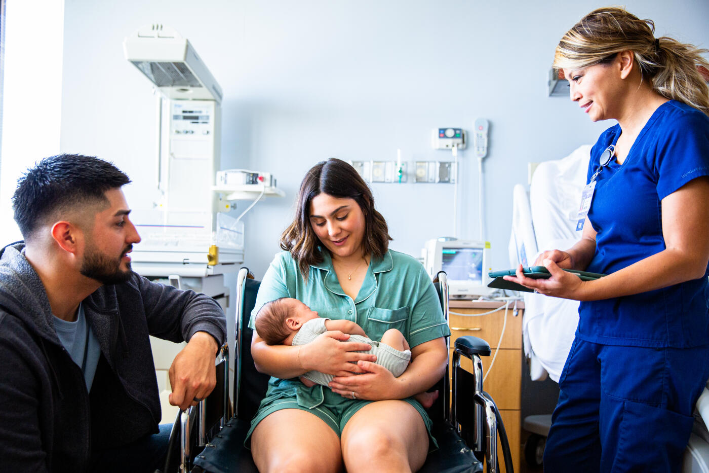 A young family consisting of a hispanic father and mother and their newborn baby boy in the hospital with grandparents, a nurse, and a pediatrician.
