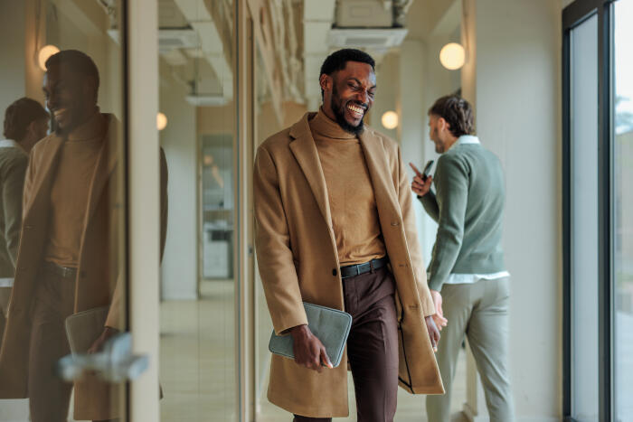 Smiling businessman walking in office corridor while his colleague is talking on the phone