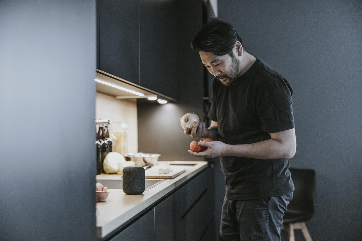 Japanese man communicating with smart speaker while cooking in the kitchen