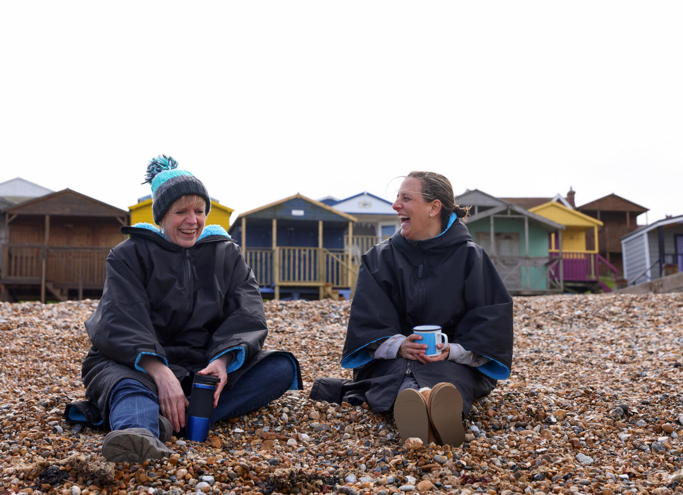 <<Two friends, wearing coats, have a conversation on the beach>>