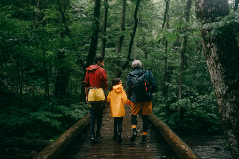 Three generation family hiking together in forest in rain