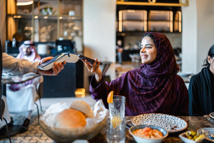 Joyful Arab Woman Settling Bill Via Smartphone in Elegant Restaurant