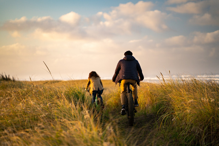 Couple ride bicycles through grassy headlands above the ocean