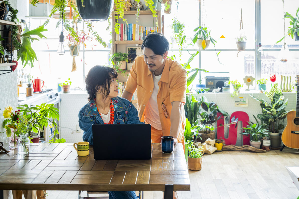 A Japanese couple collaborates on digital projects at home, surrounded by lush plants and natural light. Their lifestyle reflects sustainability, creativity, and flexible remote work.